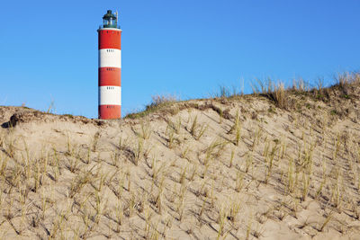 Lighthouse by sea against clear blue sky