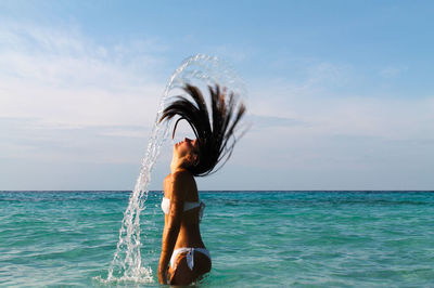 Side view of woman tossing hair in sea against sky