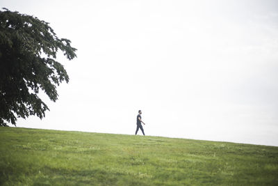 Mid distance view of young man walking on grassy land against cloudy sky