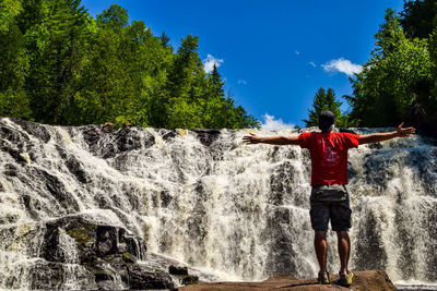 Full length of young man standing against waterfall