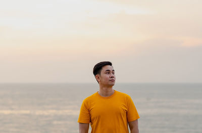 Asian man smiling and looking up with sea and sky background. good mental health concept.