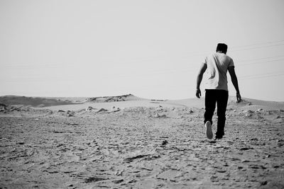 Rear view of man walking in desert against clear sky