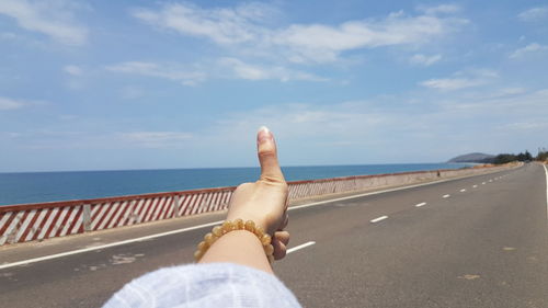 Cropped hand of woman gesturing thumbs up sign against sea