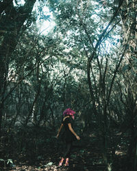 Side view of woman standing by trees in forest