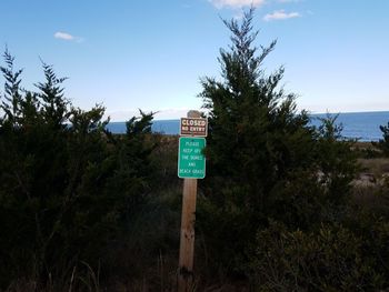 Road sign by trees against sky