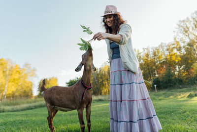 Smiling woman in a hat bonding with a goat in a rural setting