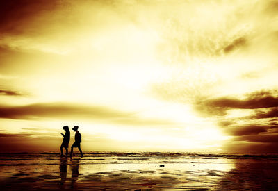 Silhouette people on beach against sky during sunset