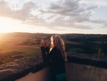 Woman photographing landscape through mobile phone during sunset