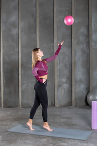 Full length of young woman exercising with arms raised standing against wall