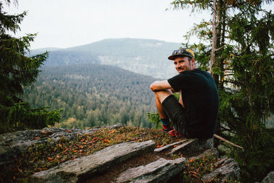 Portrait of man sitting on rock against mountains