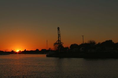 Silhouette cranes in sea against clear sky during sunset