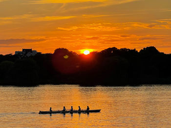 Silhouette people in river against sky during sunset