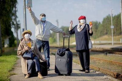Positive seniors with medical face masks waiting for a train before traveling during a pandemic