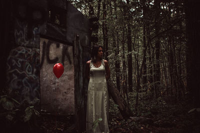 Woman with helium balloon while standing at forest