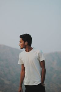 Young man looking away while standing against mountains