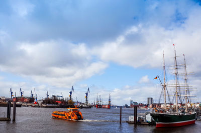 Boats moored at commercial dock in sea against cloudy sky