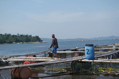 Side view of man walking on bamboos over lake