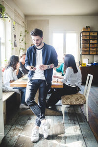 Businessman using smart phone while computer programmers having meeting at workplace