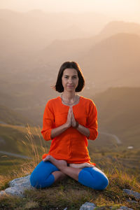 Yogini in the lotus position in full face sits on a cliff against the backdrop of the sunset sky