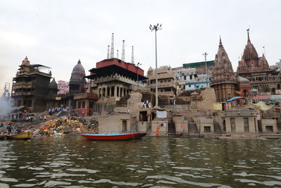 Boats in river by buildings against sky in city