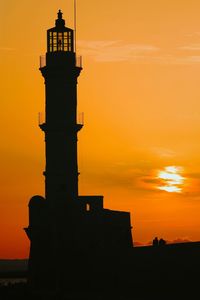 Low angle view of silhouette lighthouse against orange sky