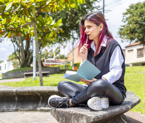 Young woman using mobile phone while sitting on tree