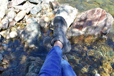 Low section of woman seated ankles crossed on rock in river