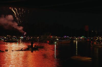 Illuminated city by river against sky at night