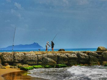 People fishing in sea against sky