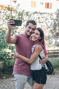 A portrait of brunette young couple smiling and taking selfie photo while walking outdoors