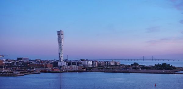 Illuminated buildings by sea against blue sky