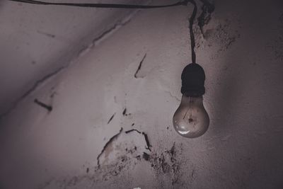 Low angle view of illuminated light bulb hanging on wall