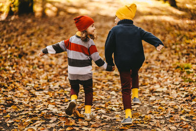 Happy cheerful children in warm clothes have fun walking running in autumn park playing with leaves