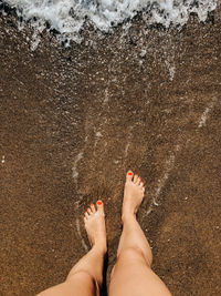 Low section of woman standing on sand at beach