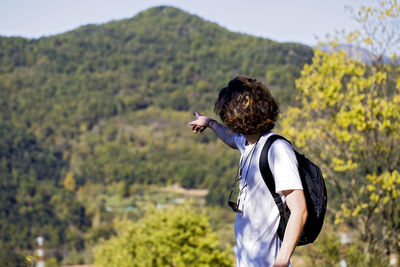 Young man pointing while standing on mountain against sky