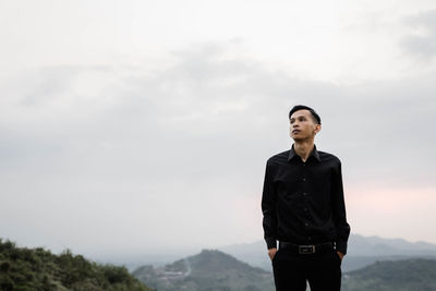 Young man looking away against sky