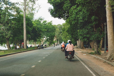 Rear view of people riding bicycle on road in city