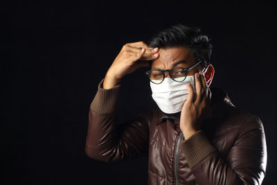 Portrait of man with headache standing against black background