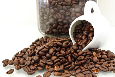 Close-up of roasted coffee beans with pitcher and jar against white background