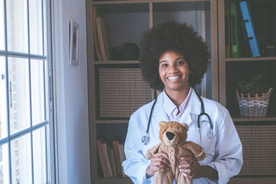 Portrait of smiling doctor holding stuffed toy at clinic