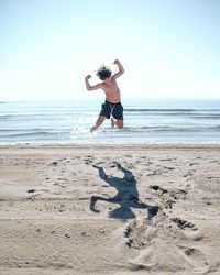 Full length of shirtless boy jumping at beach