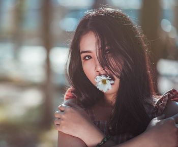 Close-up portrait of young woman carrying flower in mouth while standing at park