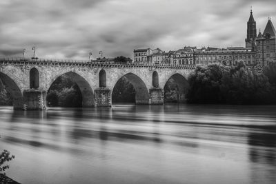 Arch bridge over river against cloudy sky