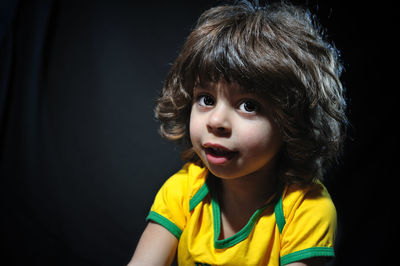 Close-up of cute boy looking away against black background