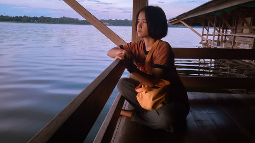 Thoughtful young woman looking away while sitting on stilt house over lake