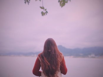 Rear view of woman standing against sky during sunset