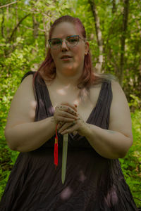 Portrait of smiling woman with arms raised in forest