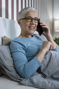 Blue-light blocking glasses. mature woman talking over the phone relaxing at home before sleep