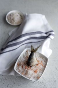 From above savory tail of marine fish sticking out from plate full of salt on white background