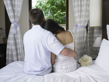 Rear view of couple sitting on bed at home